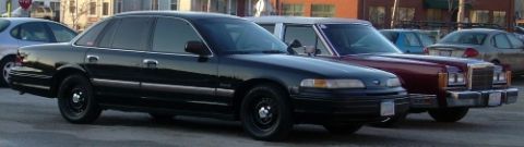 1989 Lincoln Town Car - A black Ford Crown Victoria is parked next to a maroon vehicle in a lot.