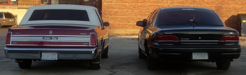 rear view of a maroon Lincoln Town Car and a black sedan parked next to each other