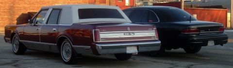 1989 Lincoln Town Car - A maroon 1989 Lincoln Town Car is parked behind a black sedan, showing their rear ends.