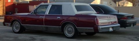 1989 Lincoln Town Car - A maroon 1989 Lincoln Town Car with a white vinyl roof is seen from a three-quarter front view, parked alongside another vehicle.