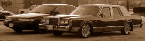 1989 Lincoln Town Car - Two sedans are parked side-by-side, one appearing to be a Lincoln Town Car from the 1980s.
