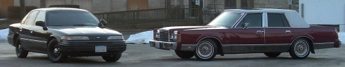Maroon 1989 Lincoln Town Car and black sedan parked on asphalt with snow in background