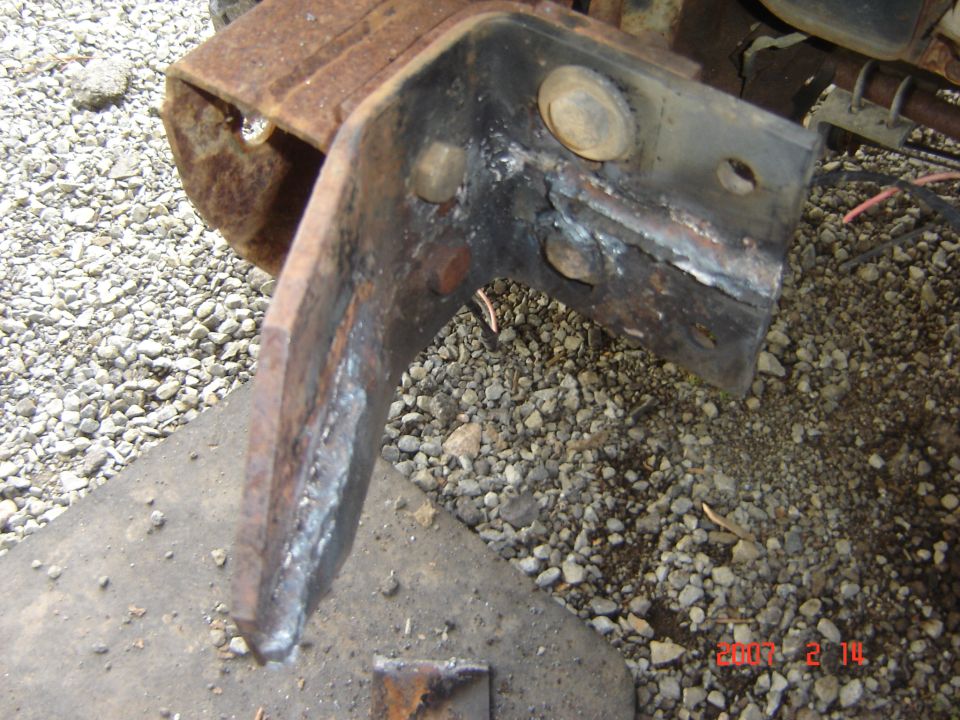 Rusted metal bracket with visible welds and bolt holes, resting on gravel