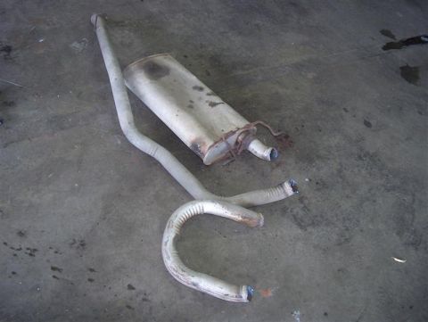 1990 Ford LTD Crown Victoria - A detached exhaust system, including a muffler and bent pipes, rests on a concrete surface.