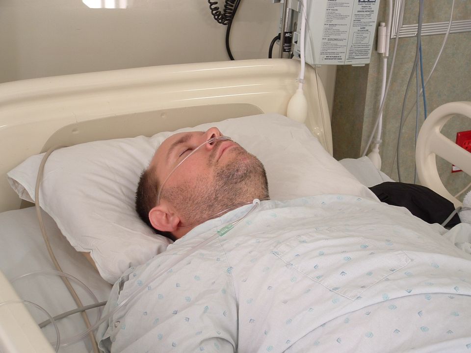 Man lying in a hospital bed with a nasal cannula and medical equipment nearby