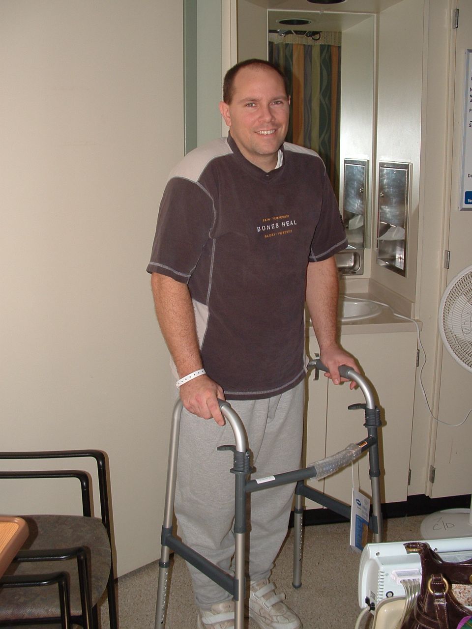 Man with hospital wristband smiling while using a walker in a hospital room