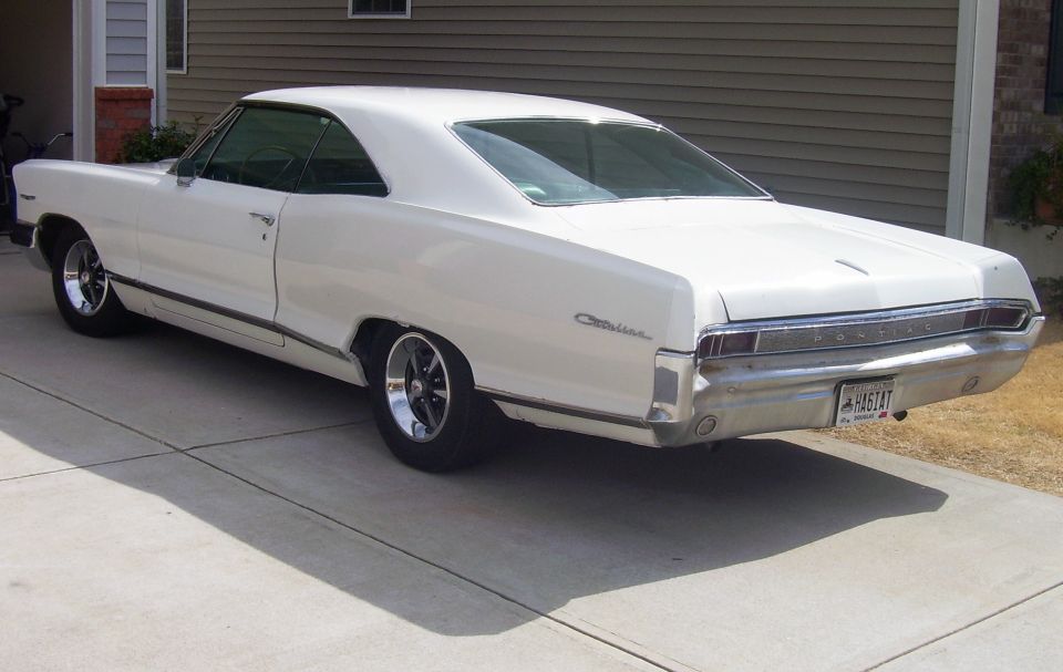White 1965 Pontiac Catalina coupe parked on a concrete driveway, rear quarter view