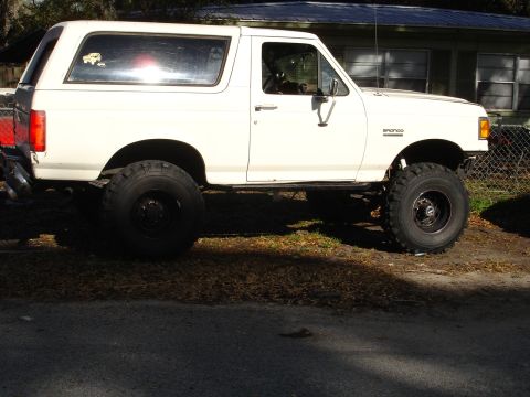 1989 Ford Bronco - A white 1989 Ford Bronco is shown lifted with large off-road tires.
