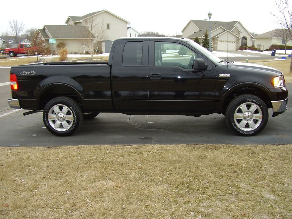Black Ford F-150 extended-cab pickup, driver-side profile, in suburban driveway