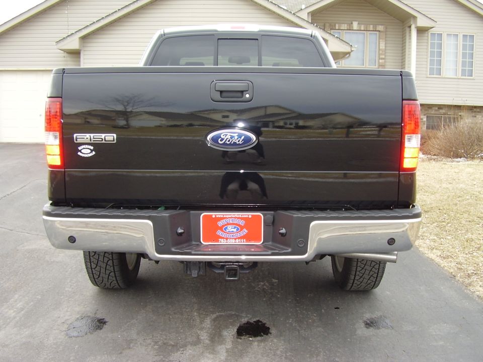 Rear view of black Ford F-150 pickup with dealer plate on driveway