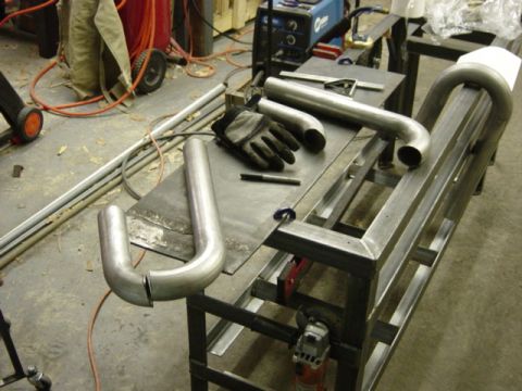 1991 Ford Bronco - Metal exhaust pipes and welding equipment are laid out on a workbench in a workshop.