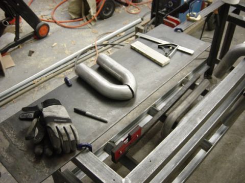 1991 Ford Bronco - A jig for bending exhaust pipes sits on a workbench with tools and a U-bend pipe.