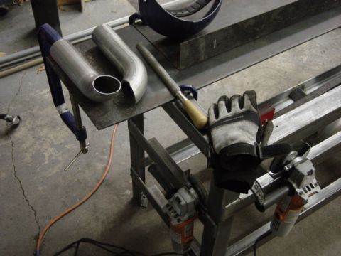 1991 Ford Bronco - Workbench setup with exhaust pipe, file, gloves, and angle grinders.