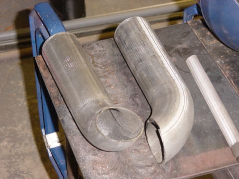 1991 Ford Bronco - Two sections of exhaust pipe are shown, one bent into a U-shape and the other into an L-shape, resting on a workbench.