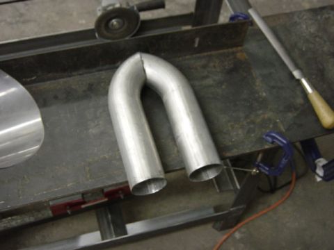 1991 Ford Bronco - A metal exhaust pipe U-bend is shown on a workbench, with tools suggesting fabrication or repair work.