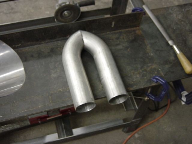 Metal exhaust pipe U-bend on a workbench with a grinder and file nearby