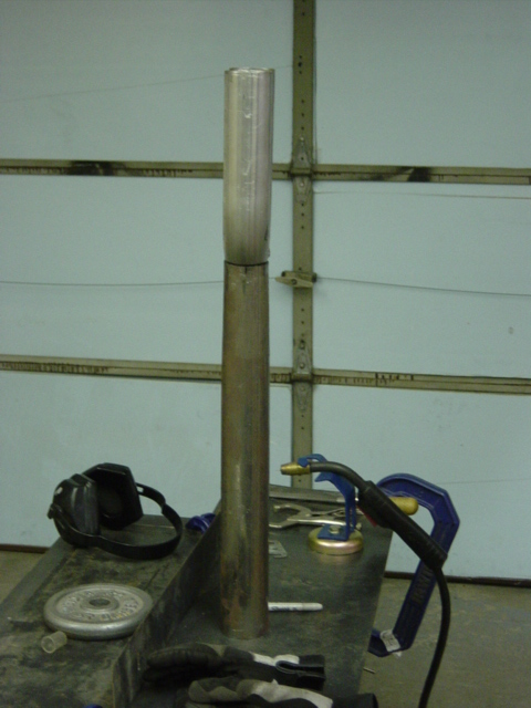 1991 Ford Bronco - A section of exhaust pipe is shown on a workbench, with welding equipment and safety gear nearby.