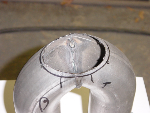 Top-down close-up of tack-welded exhaust Y-pipe merge with marker layout lines
