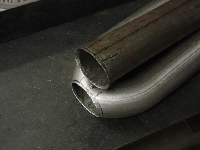 Two exhaust tubes dry-fitted and scribed for a merge cut on a steel bench