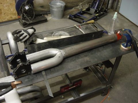 1991 Ford Bronco - Metal exhaust pipe assembly with welding equipment and tools on a workbench.