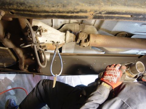 1991 Ford Bronco - A mechanic is shown working on the exhaust system of a vehicle, focusing on the driveshaft and muffler components.