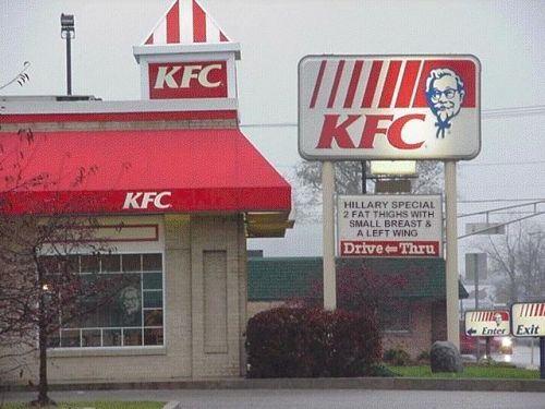 KFC restaurant with red awnings and a large sign Colonel Sanders. A drive-thru menu board is visible