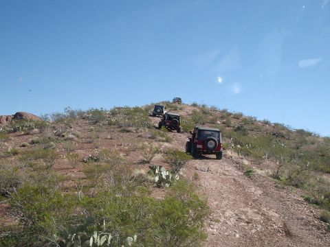 1996 Ford Bronco - A group of Jeeps navigates a , arid trail under a clear blue sky.