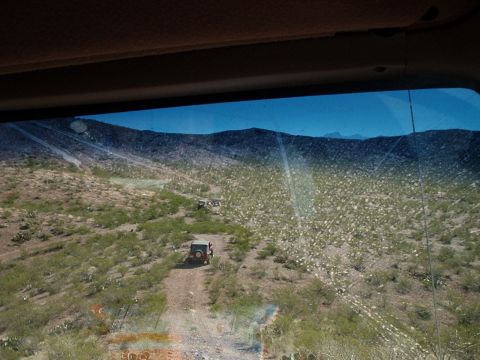 1996 Ford Bronco - Multiple off-road vehicles navigate a dusty trail through a desert environment under a clear blue sky.
