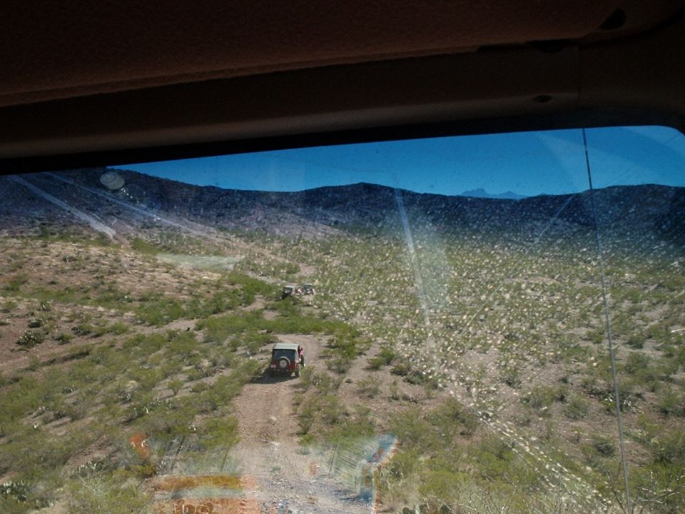 Red Jeep Wrangler on a dirt trail in a desert landscape with mountains in the background
