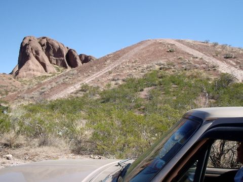 1996 Ford Bronco - A tan pickup truck is parked in a desert area with rocky hills and sparse vegetation under a clear blue sky.