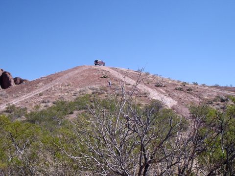 1996 Ford Bronco - A red SUV is parked on top of a dusty hill with a person walking nearby.