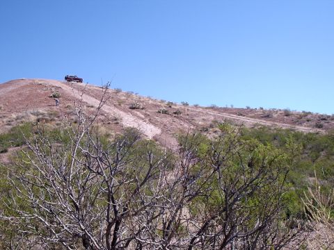 1996 Ford Bronco - A dark pickup truck is parked on a dirt road on a hill with sparse vegetation and a clear blue sky.