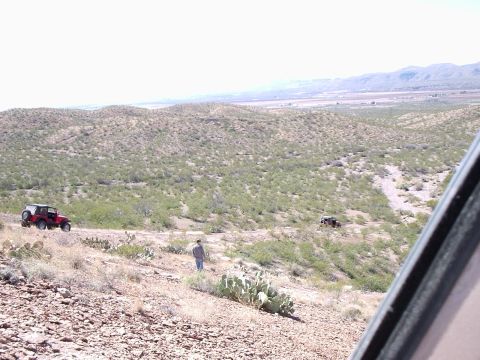 1996 Ford Bronco - Two off-road vehicles navigate a dusty trail through a dry, hilly landscape.