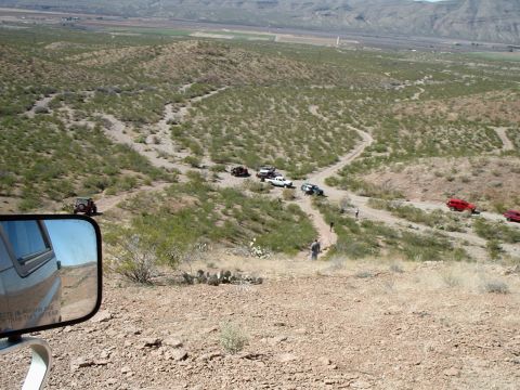 1996 Ford Bronco - Multiple off-road vehicles navigate dusty trails through a vast, arid, and hilly terrain under a clear sky.