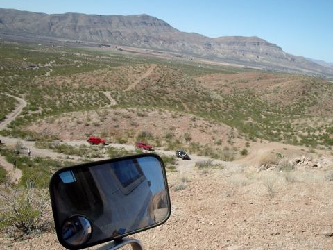 1996 Ford Bronco - Several off-road vehicles navigate a winding dirt path through a dry, mountainous landscape.