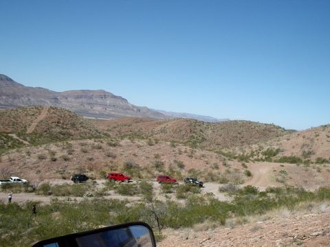1996 Ford Bronco - Several off-road vehicles traverse a dusty trail through a desert landscape under a clear blue sky.