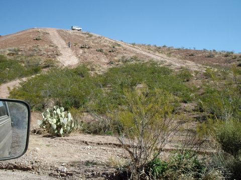 1996 Ford Bronco - A white SUV is parked on a dirt hill in a desert landscape with sparse vegetation.