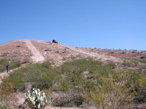 1996 Ford Bronco - A lone SUV navigates a dusty trail on a barren hillside with sparse desert vegetation.