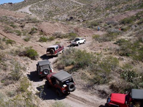 1996 Ford Bronco - Multiple off-road vehicles traverse a challenging dirt path in a dry, arid landscape.