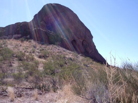 1996 Ford Bronco - A large rock formation dominates the landscape, with sparse vegetation covering the hillside under a bright, sunny sky.