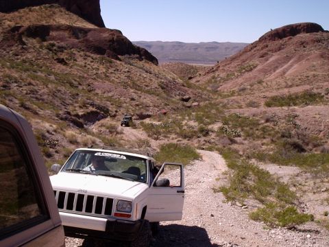 1996 Ford Bronco - Jeep convoy navigates a dusty trail through a rocky desert landscape under a clear blue sky.