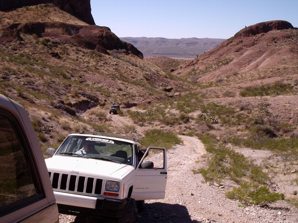 White Jeep Cherokee with door open on a desert trail, other vehicles in distance