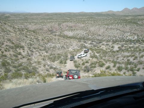 1996 Ford Bronco - A convoy of off-road vehicles navigates a dusty trail in a vast, arid terrain under a clear blue sky.
