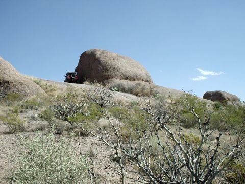 1996 Ford Bronco - A red SUV is visible on a rocky incline, surrounded by desert vegetation and large boulders.