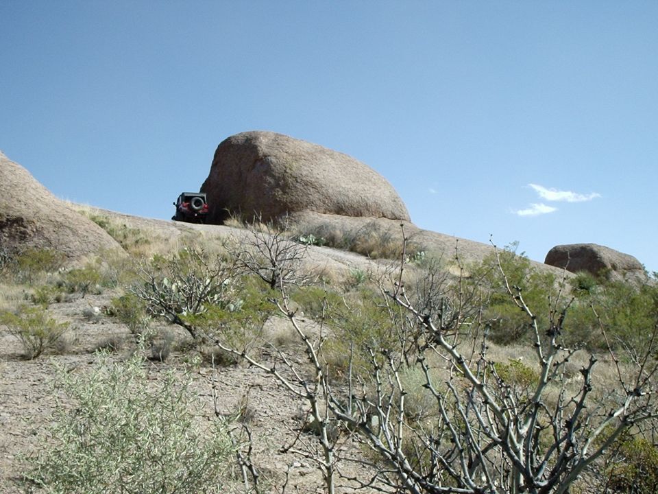 Red SUV parked on a rocky, arid hillside under a clear blue sky