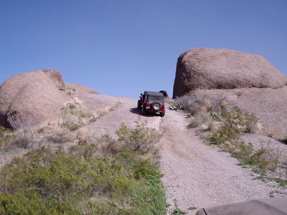 Red Jeep Wrangler driving up a rocky, off-road trail between large boulders