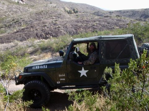 1996 Ford Bronco - A man drives a Jeep Wrangler on a dirt trail through a dry, hilly landscape.