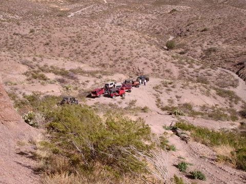 1996 Ford Bronco - Multiple off-road vehicles are stopped on a dusty trail in a dry, hilly environment.