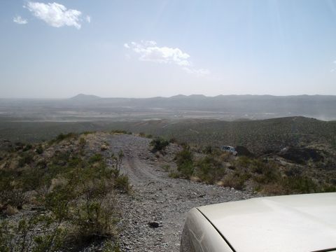 1996 Ford Bronco - Two SUVs navigate a challenging off-road path through a dry, mountainous landscape under a hazy sky.
