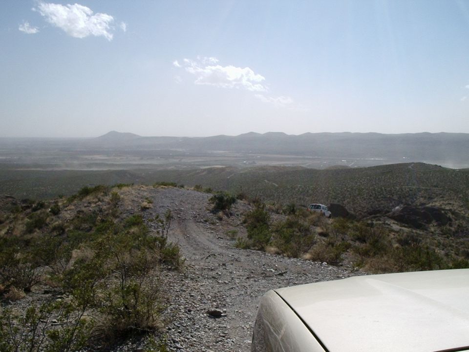 Two white SUVs on a dusty, rocky off-road trail with mountains in the distance